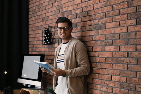 Journalist with notebook near brick wall in office