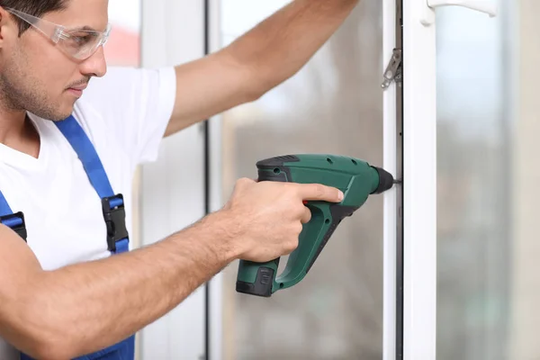 Construction worker repairing plastic window with electric screwdriver indoors