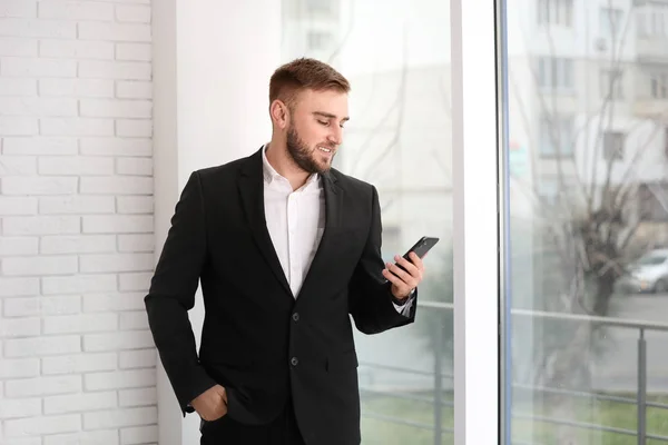 Jovem empresário usando smartphone perto da janela em casa — Fotografia de Stock