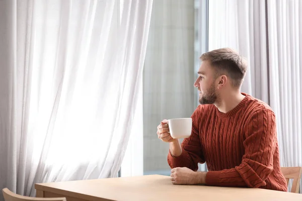 Young man with cup of hot drink near window at cafe — Stock Photo, Image