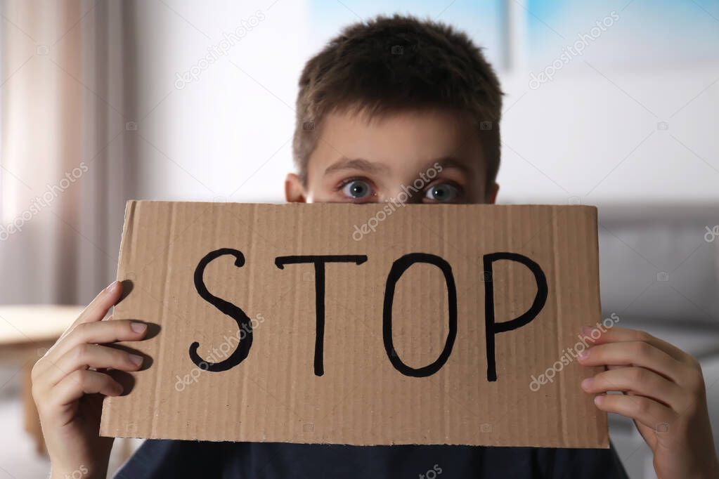 Abused little boy with sign STOP indoors. Domestic violence conc