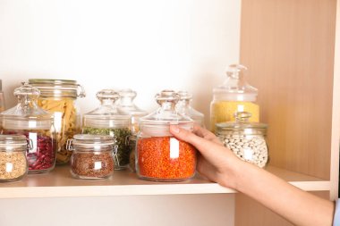Ahşap raftan bir kavanoz kırmızı mercimek alan kadın, yakın plan.
