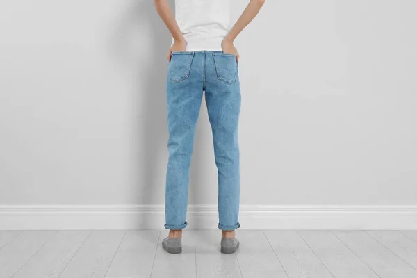 Молода жінка в стильних джинсах біля світлої стіни, крупним планом — стокове фото