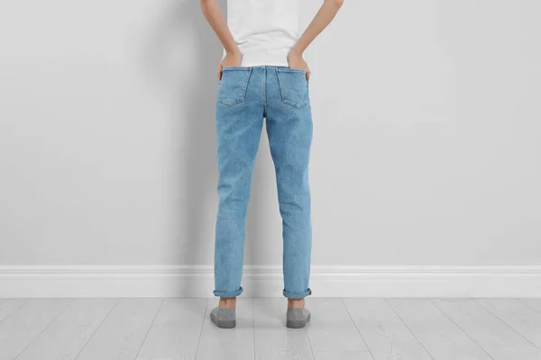 Jonge vrouw in stijlvolle jeans bij lichte wand, close-up — Stockfoto