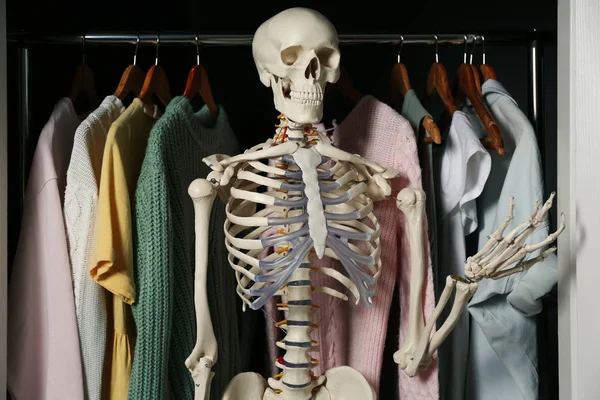 Artificial human skeleton model among clothes in wardrobe