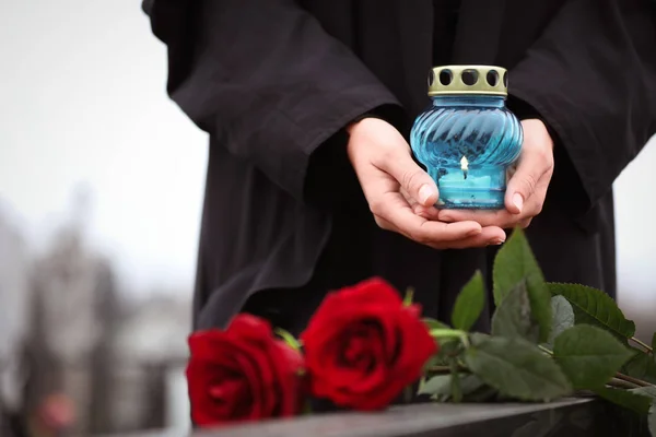 Žena drží svíčku u náhrobku s červenými růžemi venku, clo — Stock fotografie