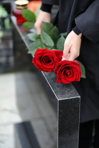 Жінка з червоними трояндами біля чорного гранітного надгробку на відкритому повітрі, закрити — стокове фото