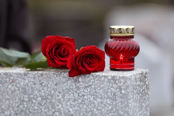 Red roses and candle on light grey tombstone outdoors. Funeral c — Stock Photo, Image