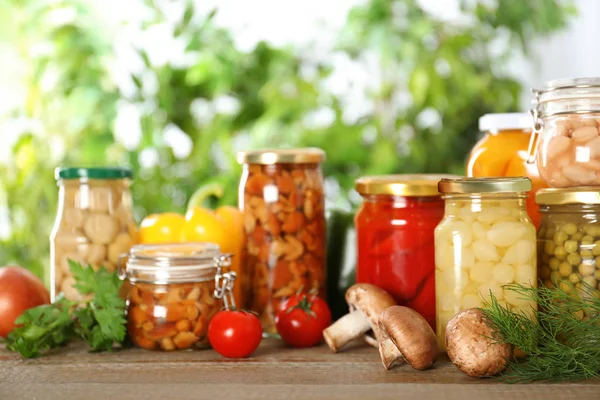 Glass jars of different pickled vegetables on wooden table — Stock Photo, Image