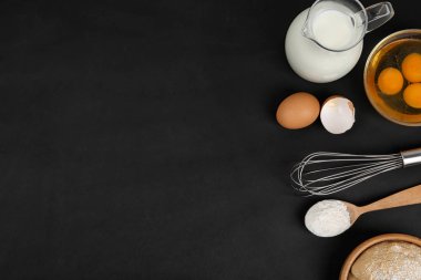 Düz kompozisyon, çiğ yumurta ve siyah arkaplan üzerindeki diğer malzemeler, metin için alan. Pasta yapmak.