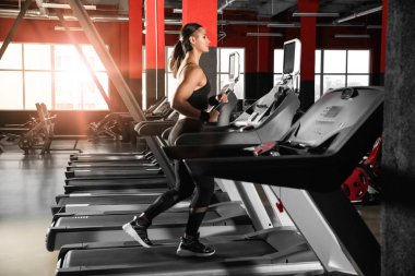 Modern spor salonunda koşu bandında çalışan genç bir kadın.