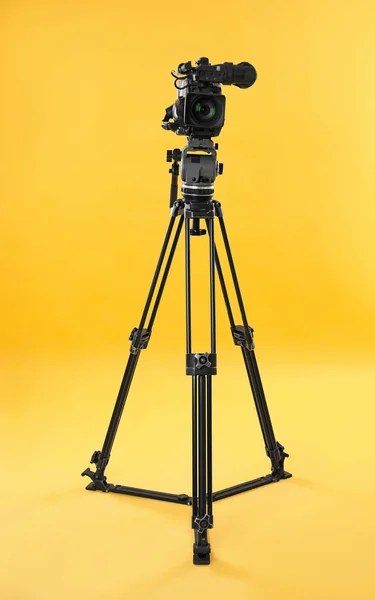 Modern professional video camera on yellow background