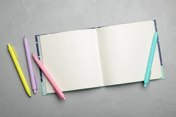 Elegante notebook aperto e penne su tavolo grigio chiaro, posa piatta — Foto Stock