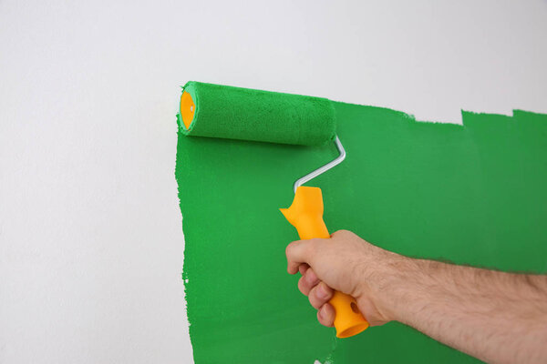 Man painting white wall with green dye, closeup. Interior renovation