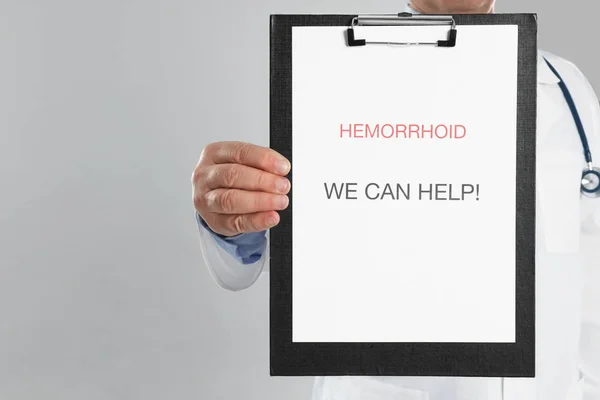 Doctor sosteniendo portapapeles con palabras HEMORRHOID que podemos ayudar en li — Foto de Stock