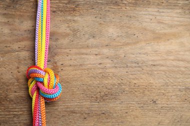 Ahşap arka planda birbirine bağlanmış renkli iplerin üst görüntüsü, metin için boşluk. Birlik kavramı