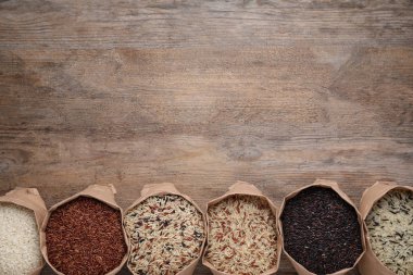 Farklı tipte kahverengi ve cilalanmış pirinçler. Tahta masadaki kağıt torbalarda, düz yerde. Metin için boşluk