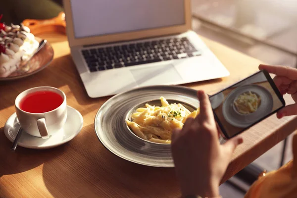 Young blogger taking picture of pasta at table in cafe, closeup