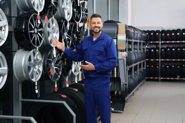 Araba lastiklerinin yanında erkek tamirci ve araba deposunda alaşım tekerlekleri var.
