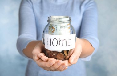 Elinde para ve etiket olan cam kavanoz tutan kadın açık mavi arka planda, yakın plan.