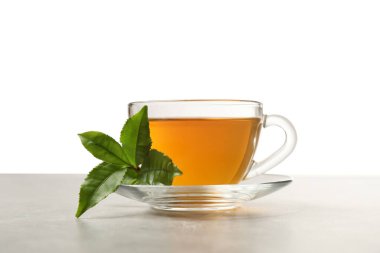 Bir fincan yeşil çay ve gri masada yapraklar.