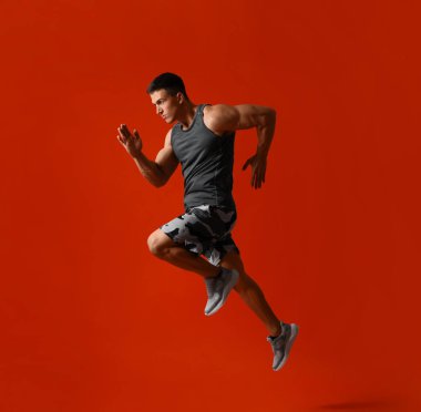 Kırmızı arka planda koşan atletik genç adam, yan görünüm