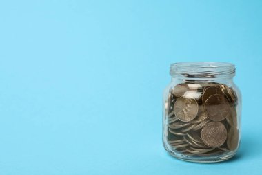 Açık mavi zemin üzerinde bozuk paralar olan cam kavanoz, metin için boşluk