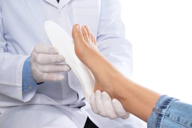 Male orthopedist fitting insole on patient's foot against white  clipart