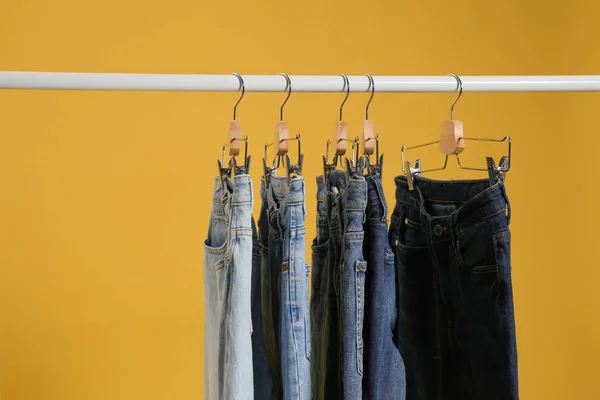 Rack with different jeans on yellow background — Stock Photo, Image