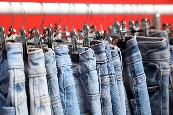 Rack with stylish jeans on red background, closeup — 스톡 사진