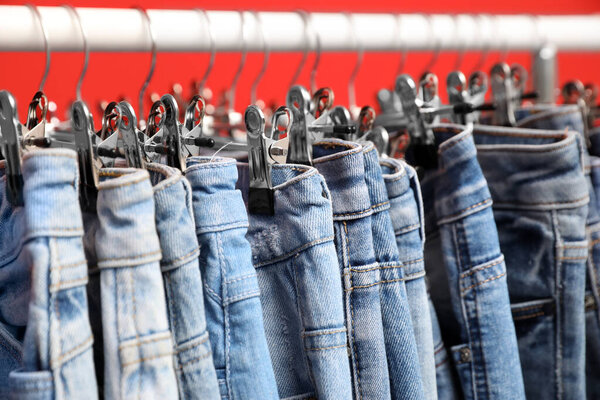 Rack with stylish jeans on red background, closeup