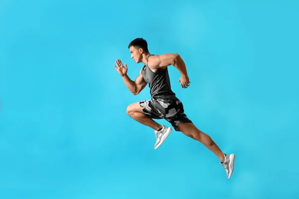 Atletisk ung man kör på ljusblå bakgrund, sidovy — Stockfoto