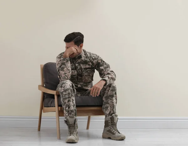 Gestresste militaire officier zit in fauteuil in de buurt van witte muur in — Stockfoto