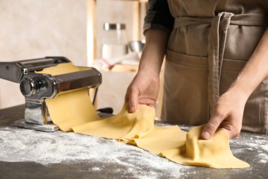 Gri masada hamuru makarna makinesiyle hazırlayan kadın.