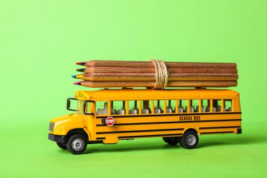 Yeşil arka planda renkli kalemleri olan okul otobüsü modeli. Aktarım