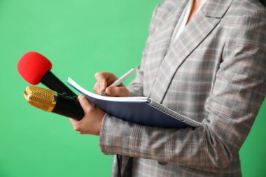 Yeşil arka planda mikrofon ve not defteri olan gazeteci, yakın plan