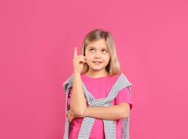Şirin küçük kız pembe arka planda günlük kıyafetler giyiyor.