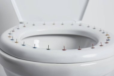 Toilet bowl with pins on white background, closeup. Hemorrhoids concept clipart