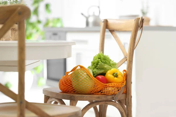 Net bag with vegetables on wooden chair in kitchen — 스톡 사진