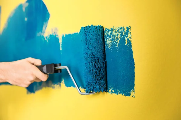 Mężczyzna malujący żółtą ścianę z niebieskim barwnikiem, zbliżenie — Zdjęcie stockowe