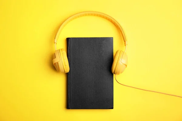 Boek en moderne koptelefoon op gele achtergrond, bovenaanzicht — Stockfoto