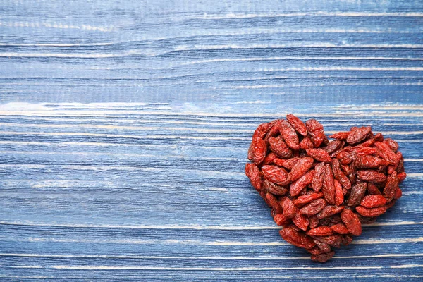 Pila en forma de corazón de bayas de goji secas sobre fondo de madera azul — Foto de Stock