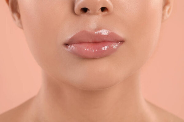 Young woman with beautiful full lips on peach background, closeup
