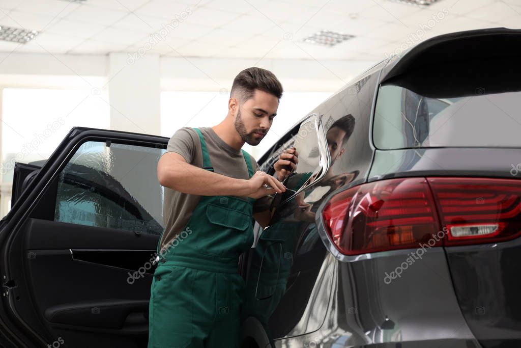 Worker tinting car window with foil in workshop