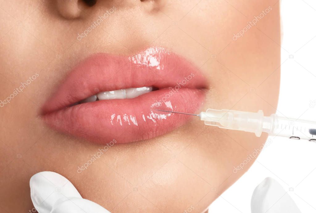 Young woman getting lips injection on white background, closeup