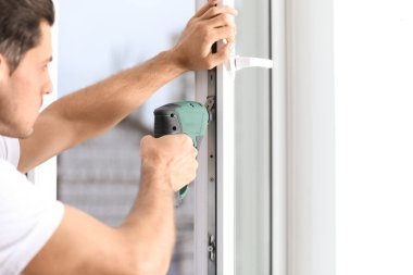 İnşaat işçisi plastik pencereyi tornavidayla tamir ediyor.