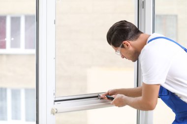 İnşaat işçisi içeride tornavidayla plastik pencereyi tamir ediyor.