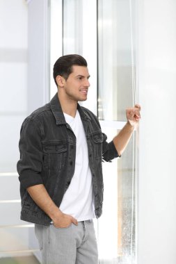 Evin penceresinin yanında günlük kıyafetler giyen yakışıklı bir adam.