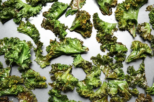 Tasty baked kale chips on grey table, flat lay