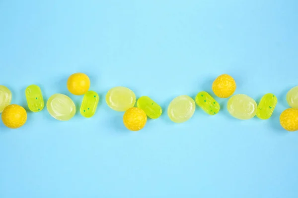 Delicious lemon candies on light blue background, flat lay